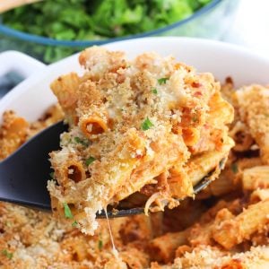 A serving spoon lifting out a scoop of baked pasta from the baking dish.