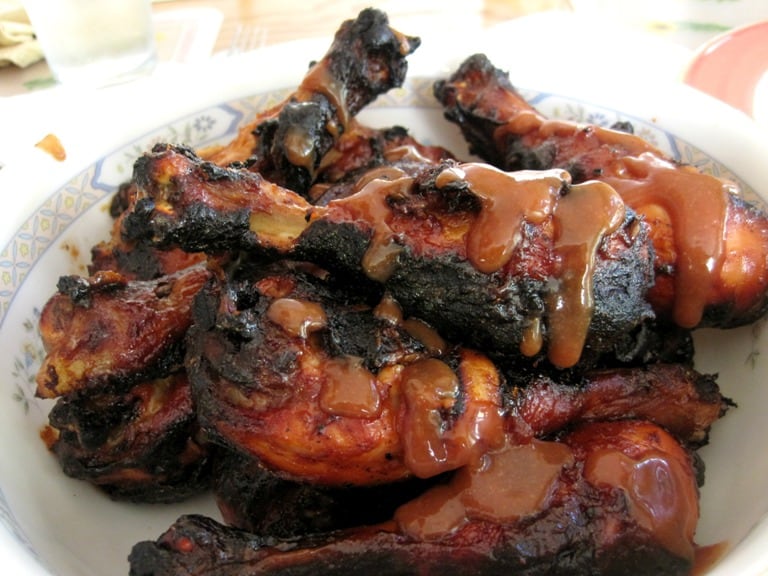 Grilled chicken drumsticks in a bowl drizzled with BBQ sauce.