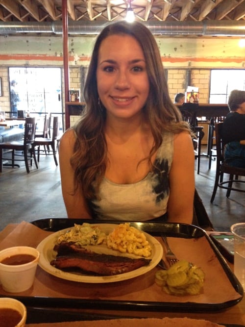 A woman smiling in front of a full plate of BBQ.