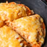 A buffalo chicken tortilla pie in a cast iron skillet cut into four quarters.