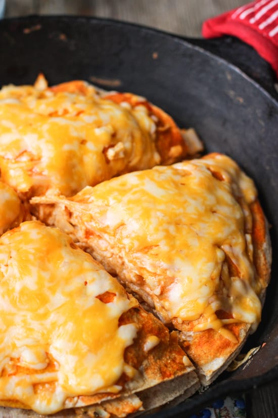 A buffalo chicken tortilla pie in a cast iron skillet cut into four quarters.