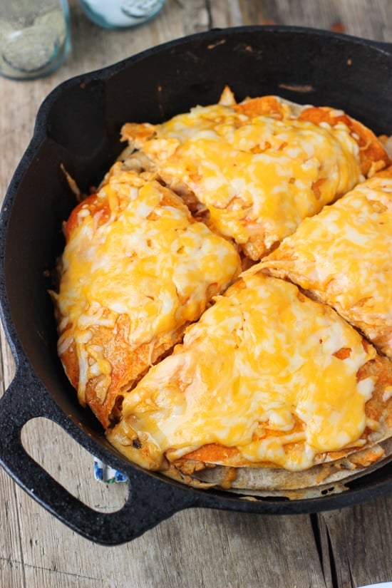 A buffalo chicken tortilla pie in a cast iron skillet cut into four quarters.