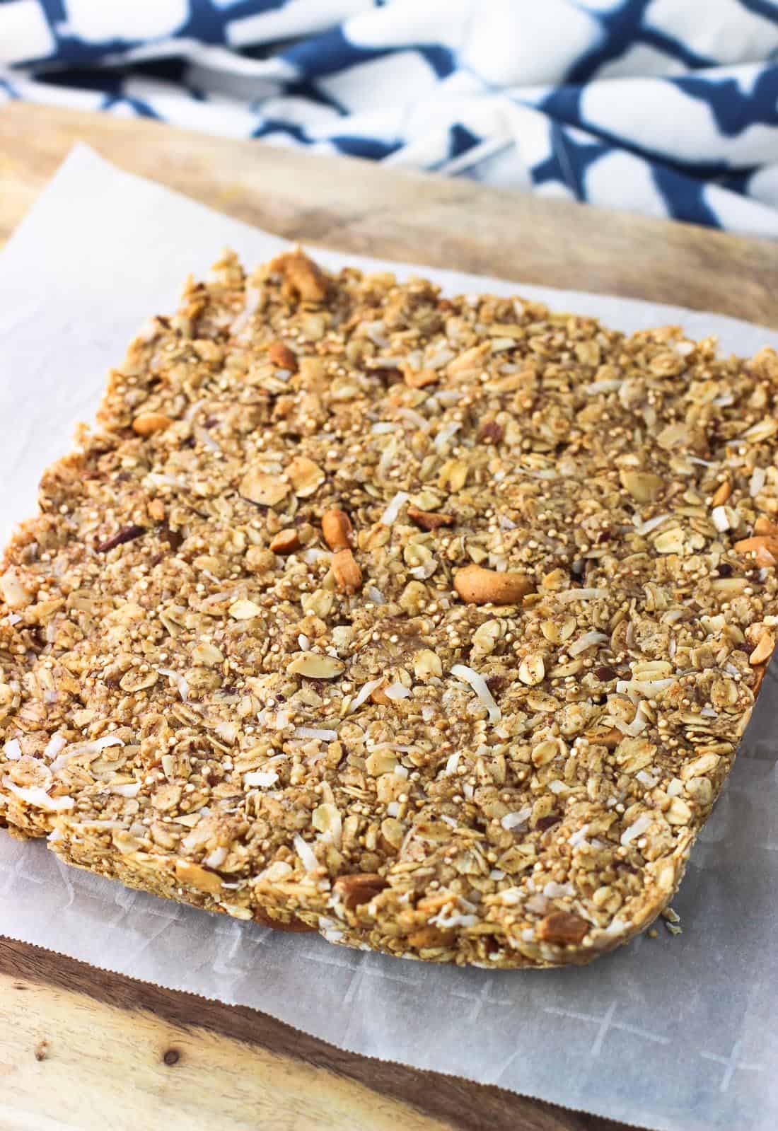 The square granola bar mixture on a parchment-lined cutting board before being cut into slices