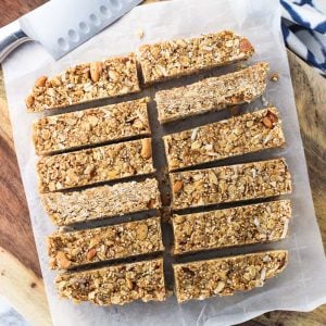 Twelve granola bars sliced on a sheet of parchment paper on a wooden board