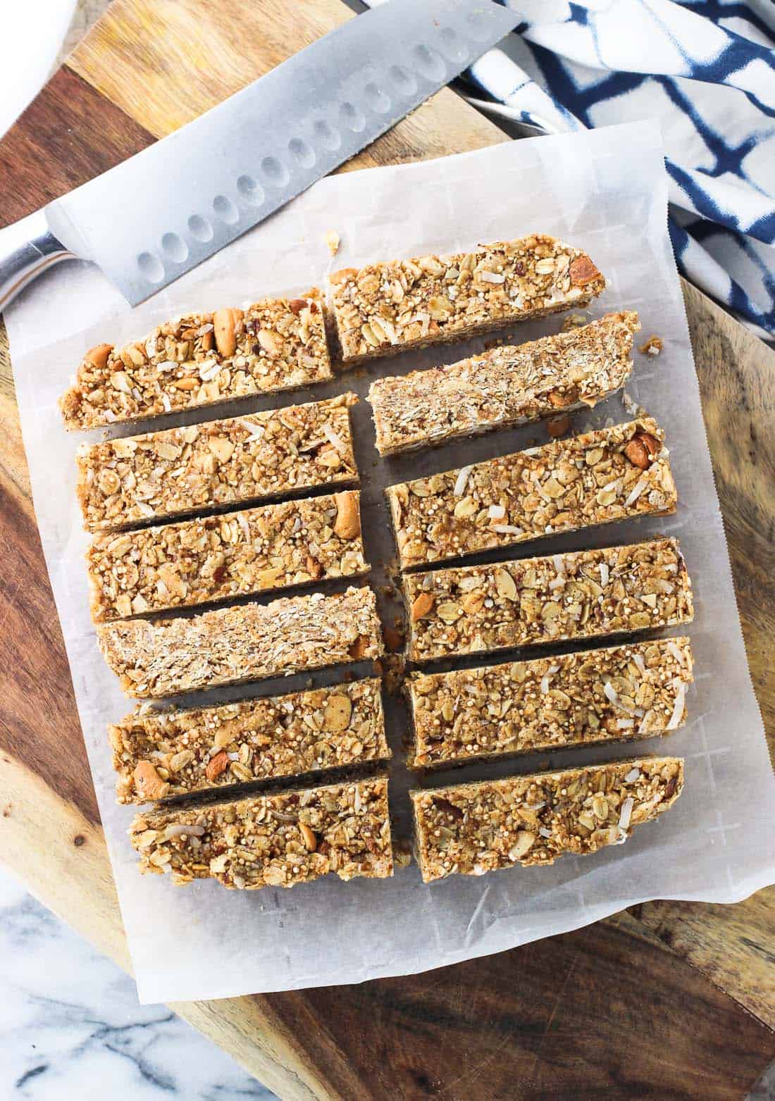 Twelve granola bars sliced on a sheet of parchment paper on a wooden board