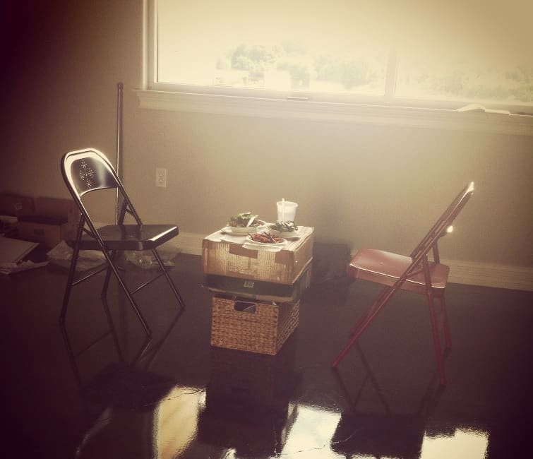 Two folding chairs with a box as a table in an empty apartment.