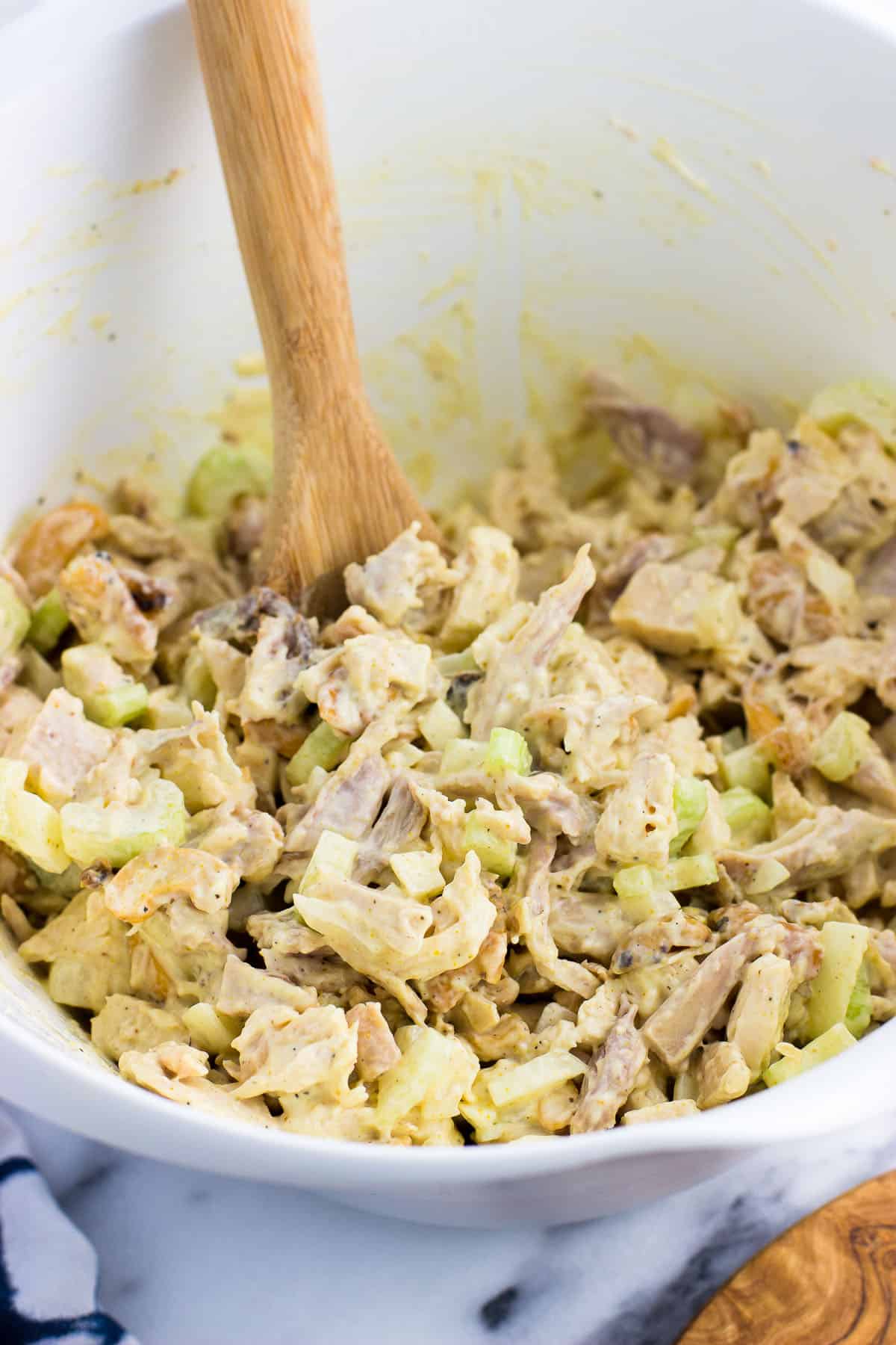 Mixed together chicken salad in a large plastic bowl with a wooden spoon in it.