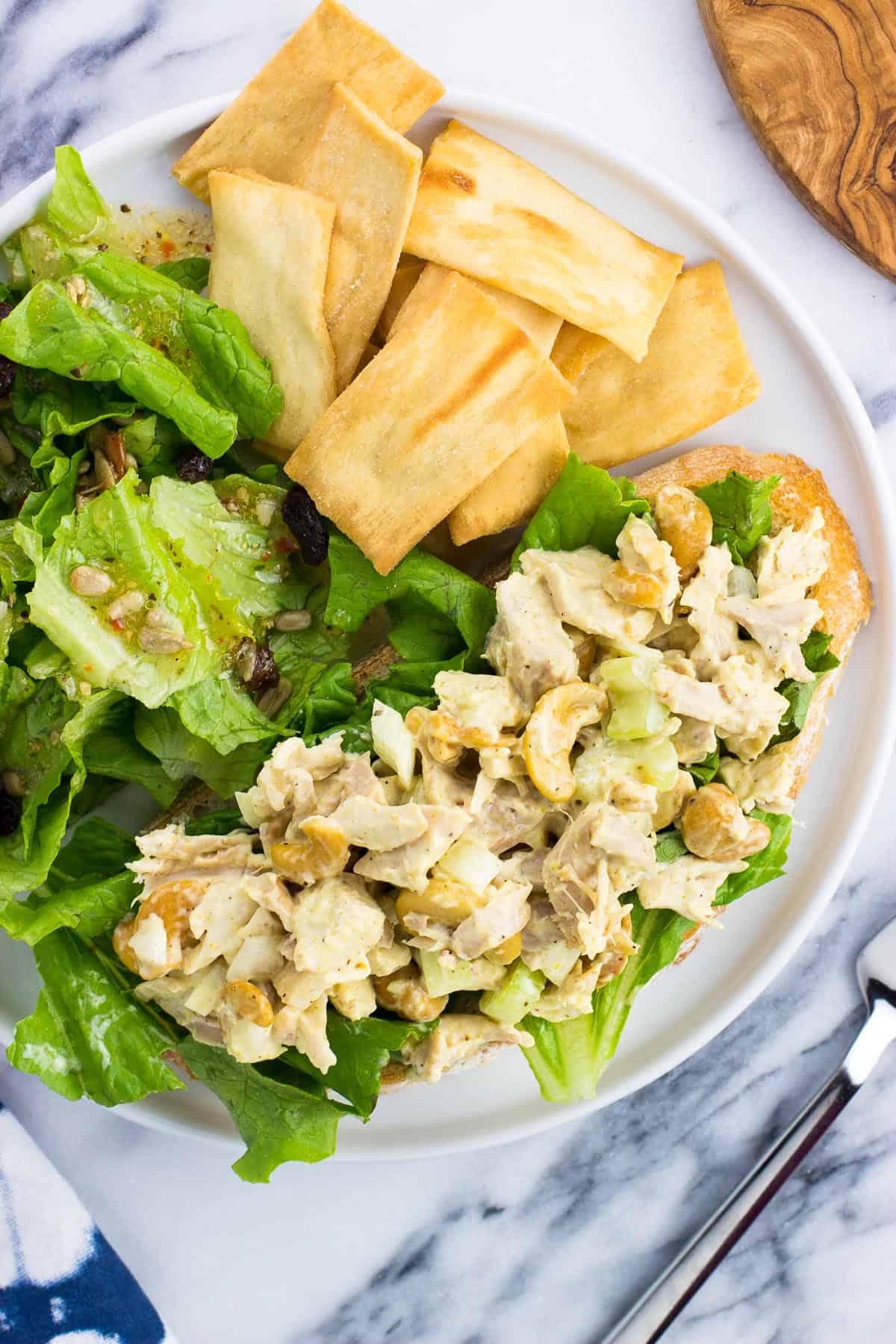 An overhead picture of a chicken salad sandwich with a side salad and pita chips.