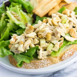 An open-face chicken salad sandwich next to a side salad and pita chips.