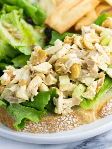 An open-face chicken salad sandwich next to a side salad and pita chips.