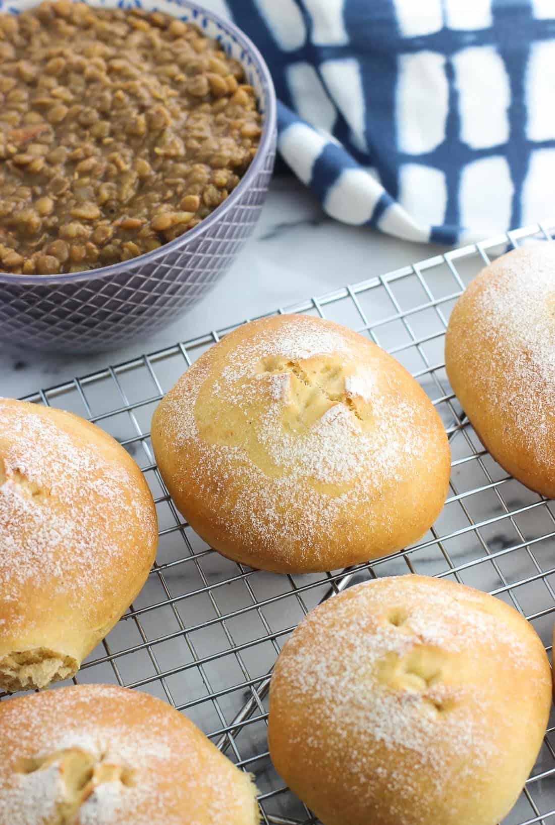 Rolls on a wire rack in front of a dish towel and a bowl of lentil soup