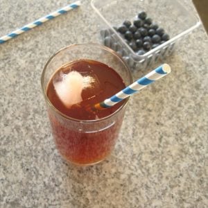 A glass of iced tea on a counter with a carton of blueberries.