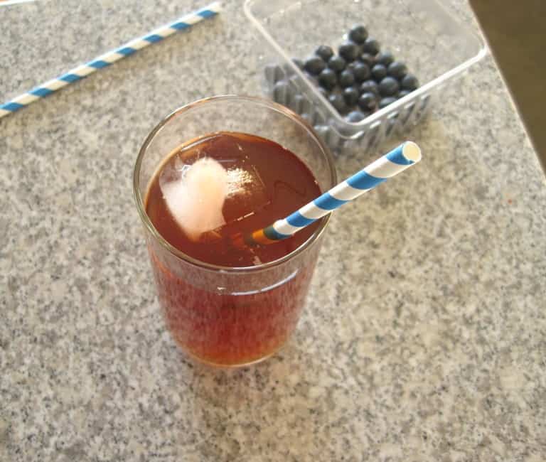 A glass of iced tea on a counter with a paper straw in it.