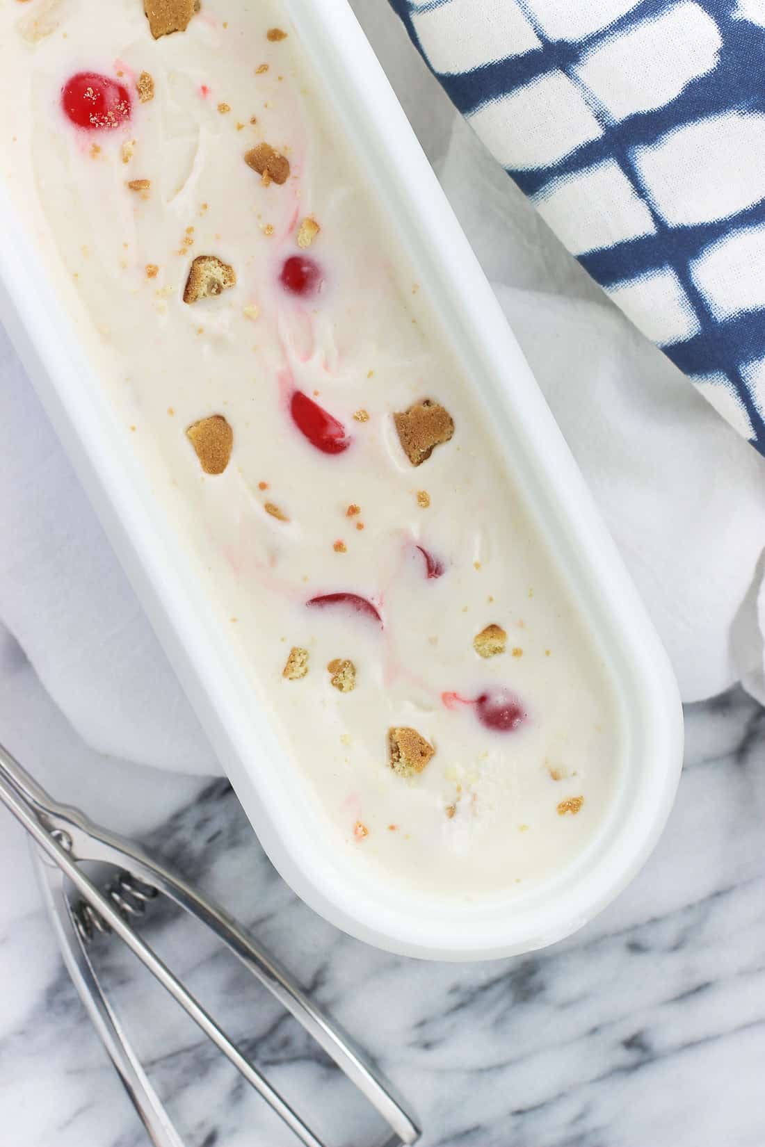 An oblong plastic container of frozen yogurt next to a metal scoop.