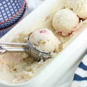 A metal scoop filled with rounded frozen yogurt in the full container.