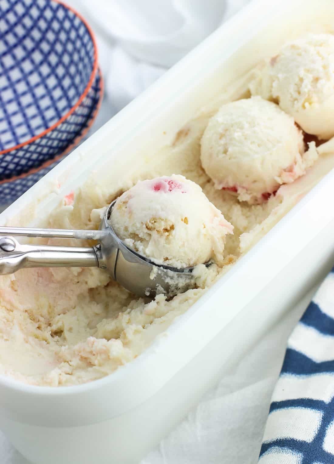 A metal scoop filled with rounded frozen yogurt in the full container.