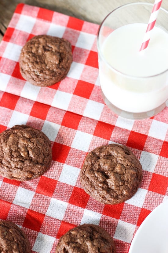 Three chocolate cookies on a cloth napkin next to a glass of milk.