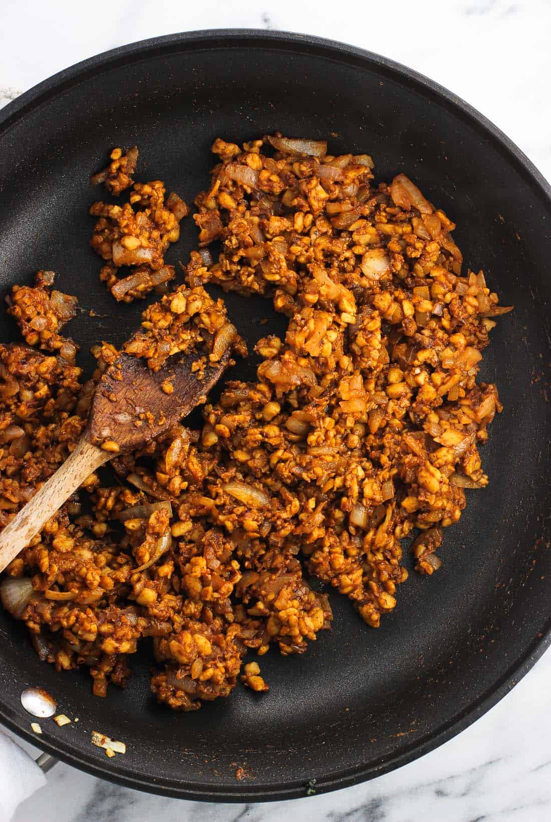 An overhead picture of crumbled seasoned tempeh in a pan with a wooden spoon.