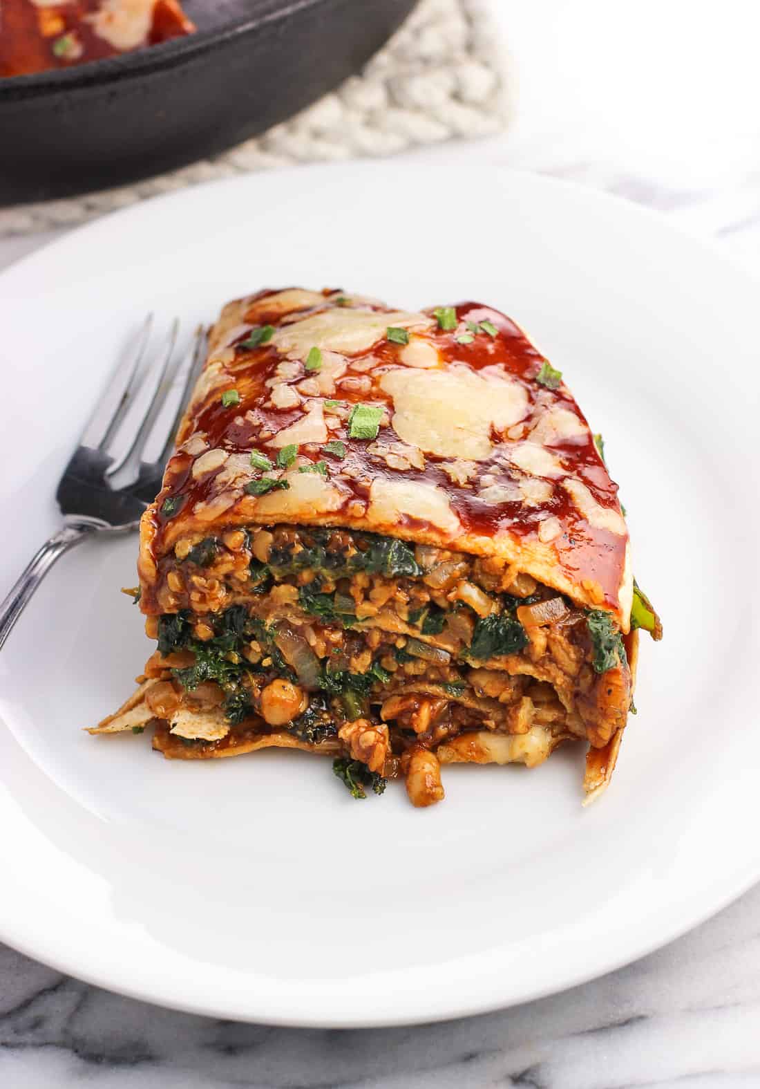 A wedge of tortilla pie on a plate with a fork with the pan in the background.