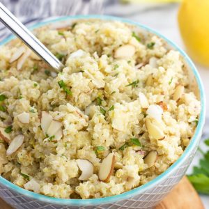 A bowl of quinoa with a spoon next to a lemon and herbs.