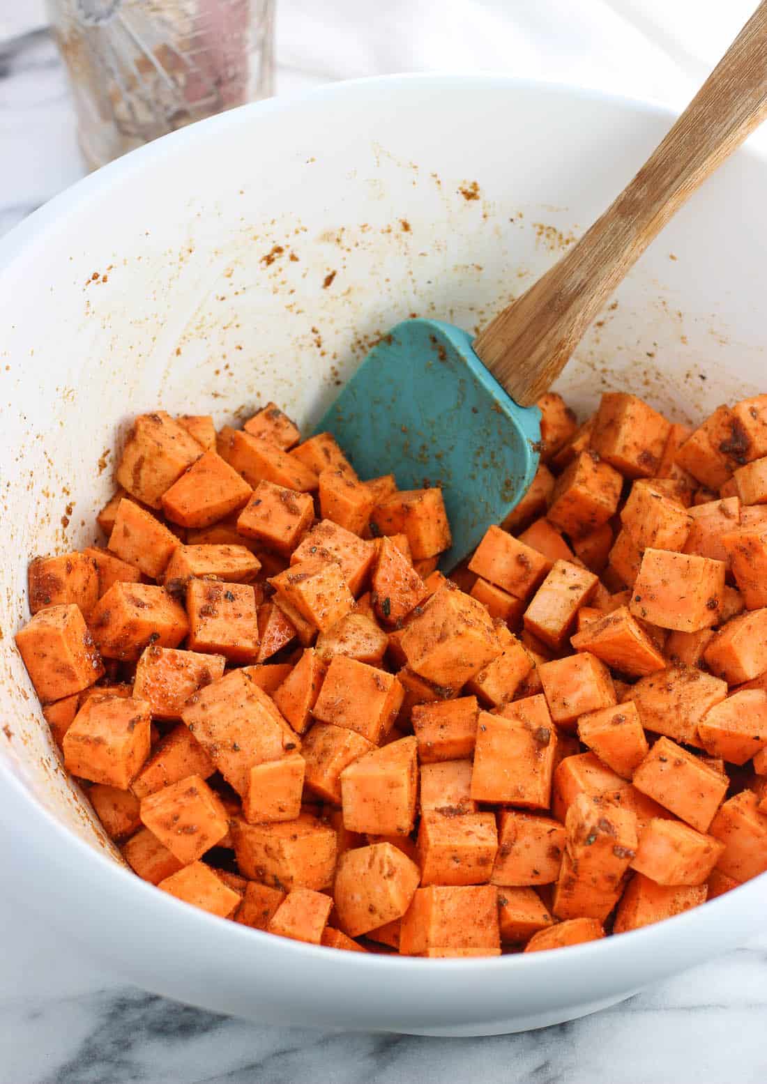 Spiced and cubed sweet potatoes in a large mixing bowl with a spatula.