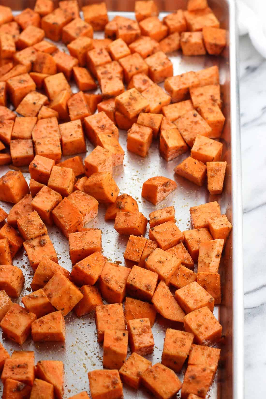 Sweet potato cubes spread onto a rimmed baking sheet in a single layer.