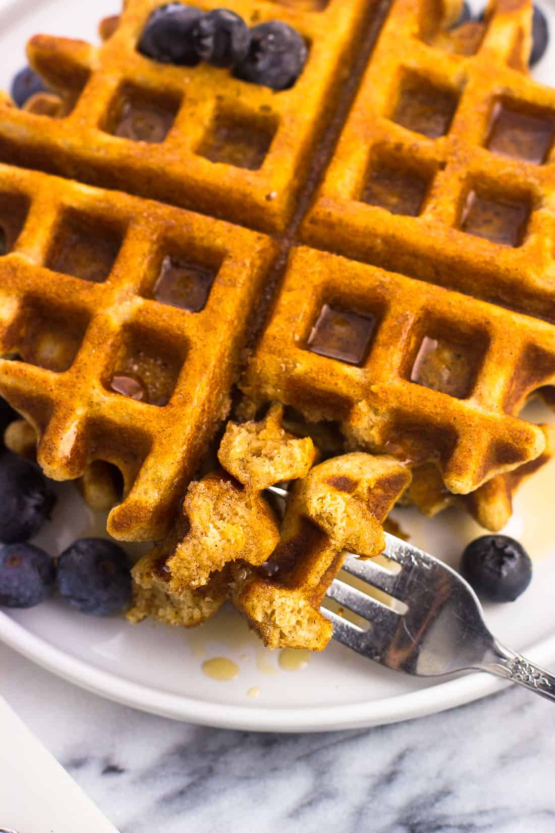 A forkful of waffle on a plate with maple syrup and blueberries