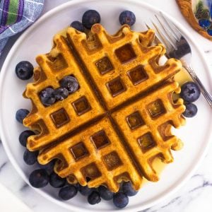 Waffles on a plate served with a maple syrup drizzle and fresh blueberries