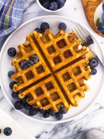 Waffles on a plate served with a maple syrup drizzle and fresh blueberries