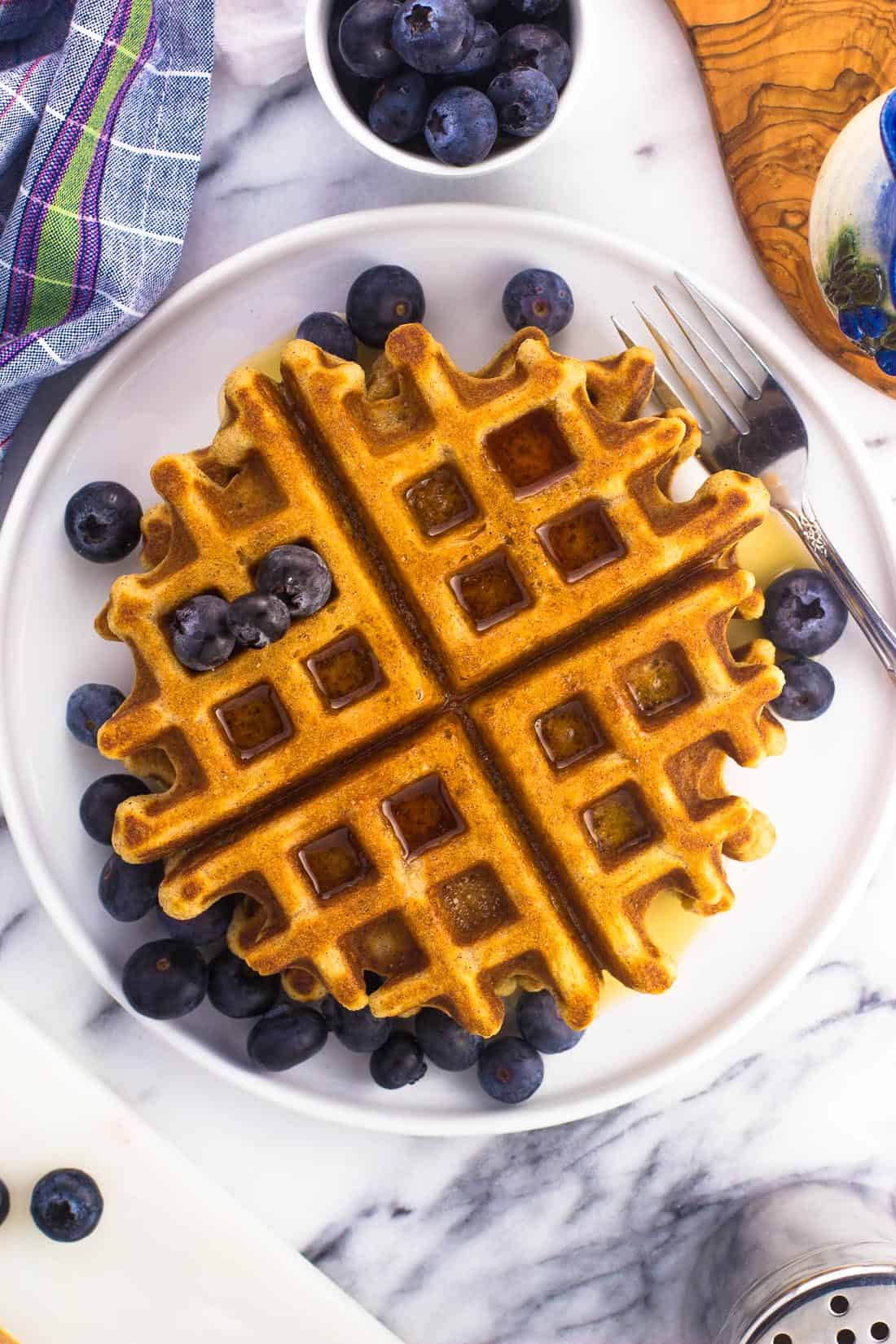 Waffles on a plate served with a maple syrup drizzle and fresh blueberries