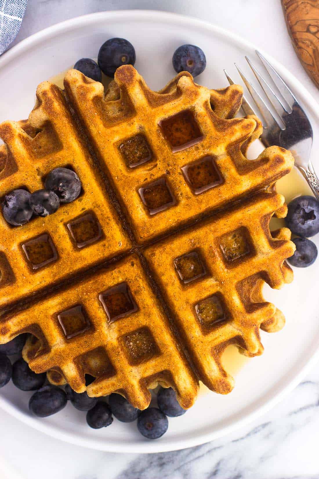 An overhead shot of waffles on a plate with maple syrup and fresh blueberries