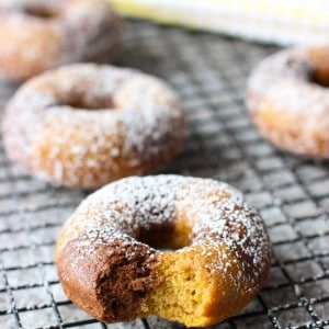 Powdered sugar-dusted donuts on a wire rack with a bite taken out of the front one.