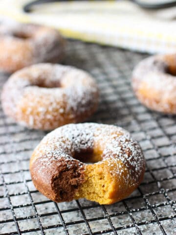 Powdered sugar-dusted donuts on a wire rack with a bite taken out of the front one.