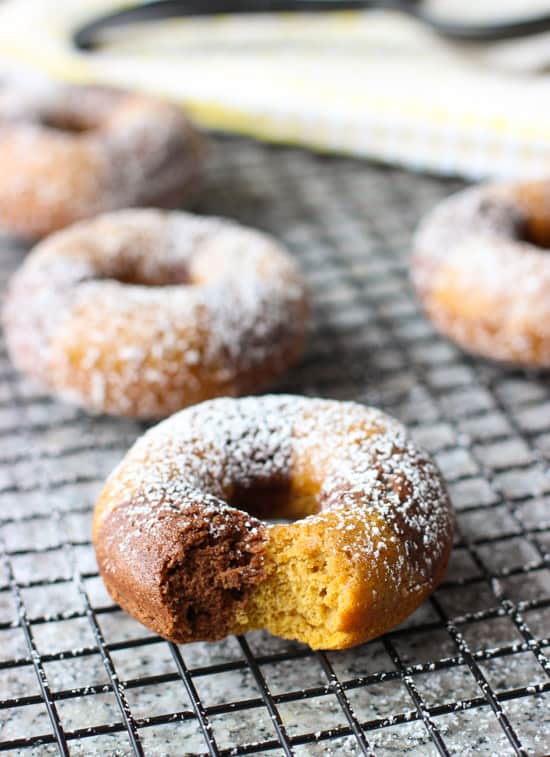 Powdered sugar-dusted donuts on a wire rack with a bite taken out of the front one.