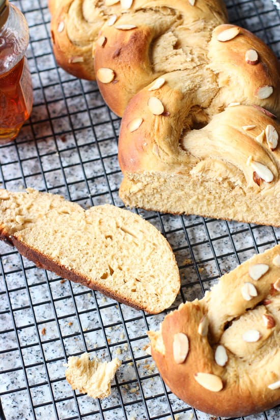 A cut loaf of bread on a wire rack with a slice laying next to it along with a bottle of honey