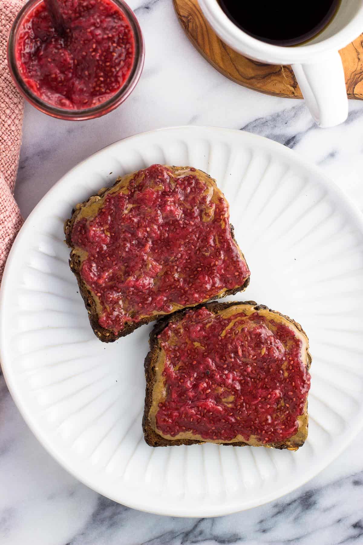 Two pieces of toast on a plate topped with jam and almond butter.