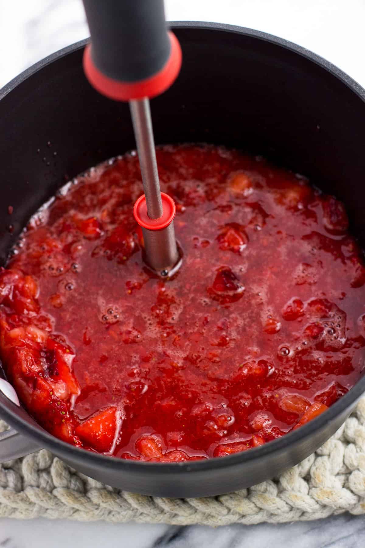 A potato masher in the saucepan having mashed the strawberries.