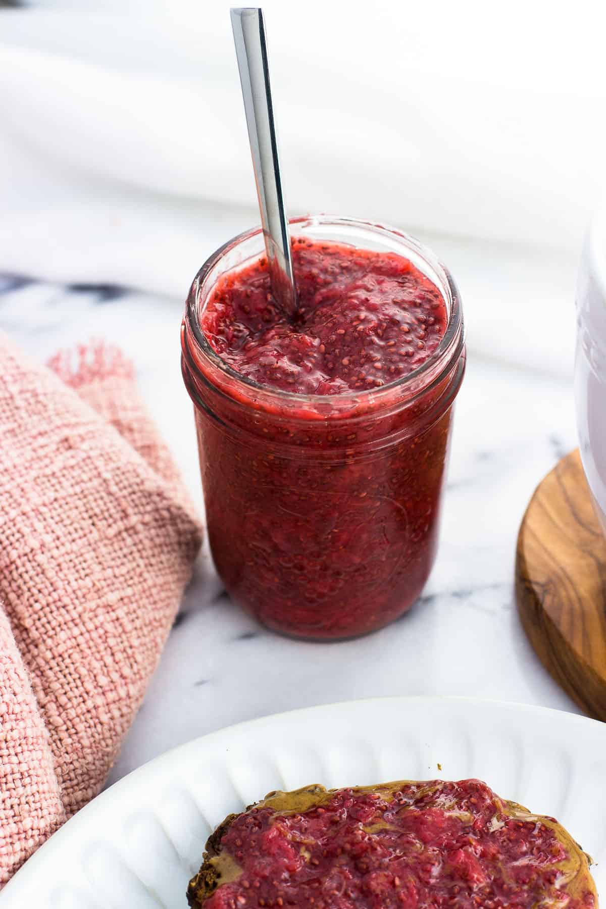 A jar of strawberry chia jam with a spoon in it.