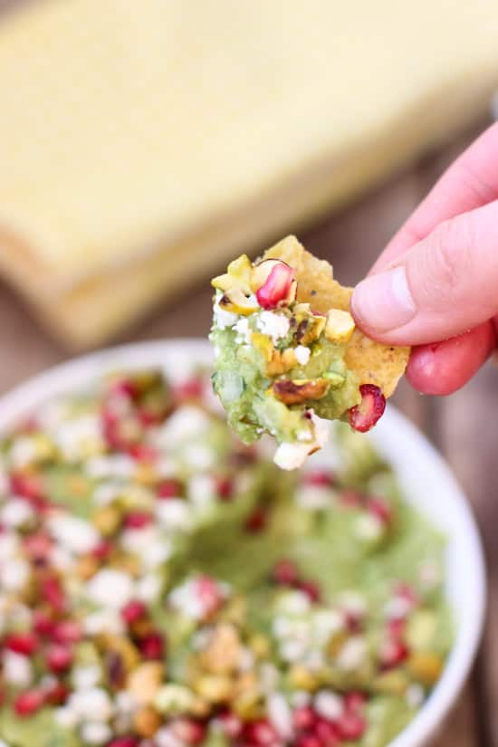 A hand scooping and lifting guacamole on a tortilla chip.