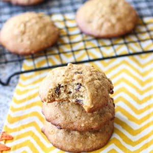 A stack of loaded oatmeal cookies on a table in front of the rest on a wire rack.