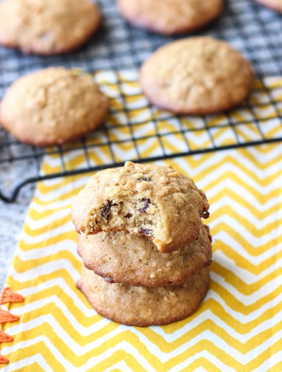 A stack of three cookies in from of a cooling rack of them with a bite taken out of the top cookie.