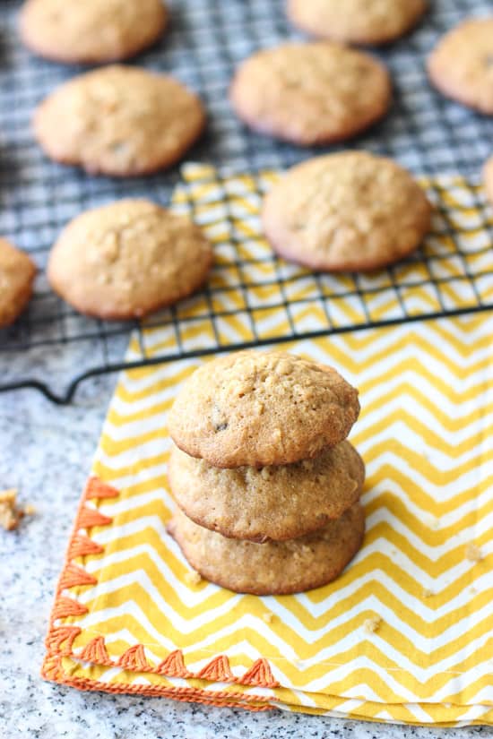 A stack of three cookies in from of a cooling rack of them.