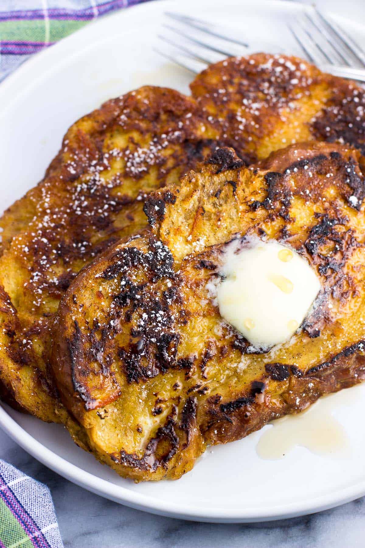 Two large slices of challah french toast on a plate with maple syrup and a pat of butter.