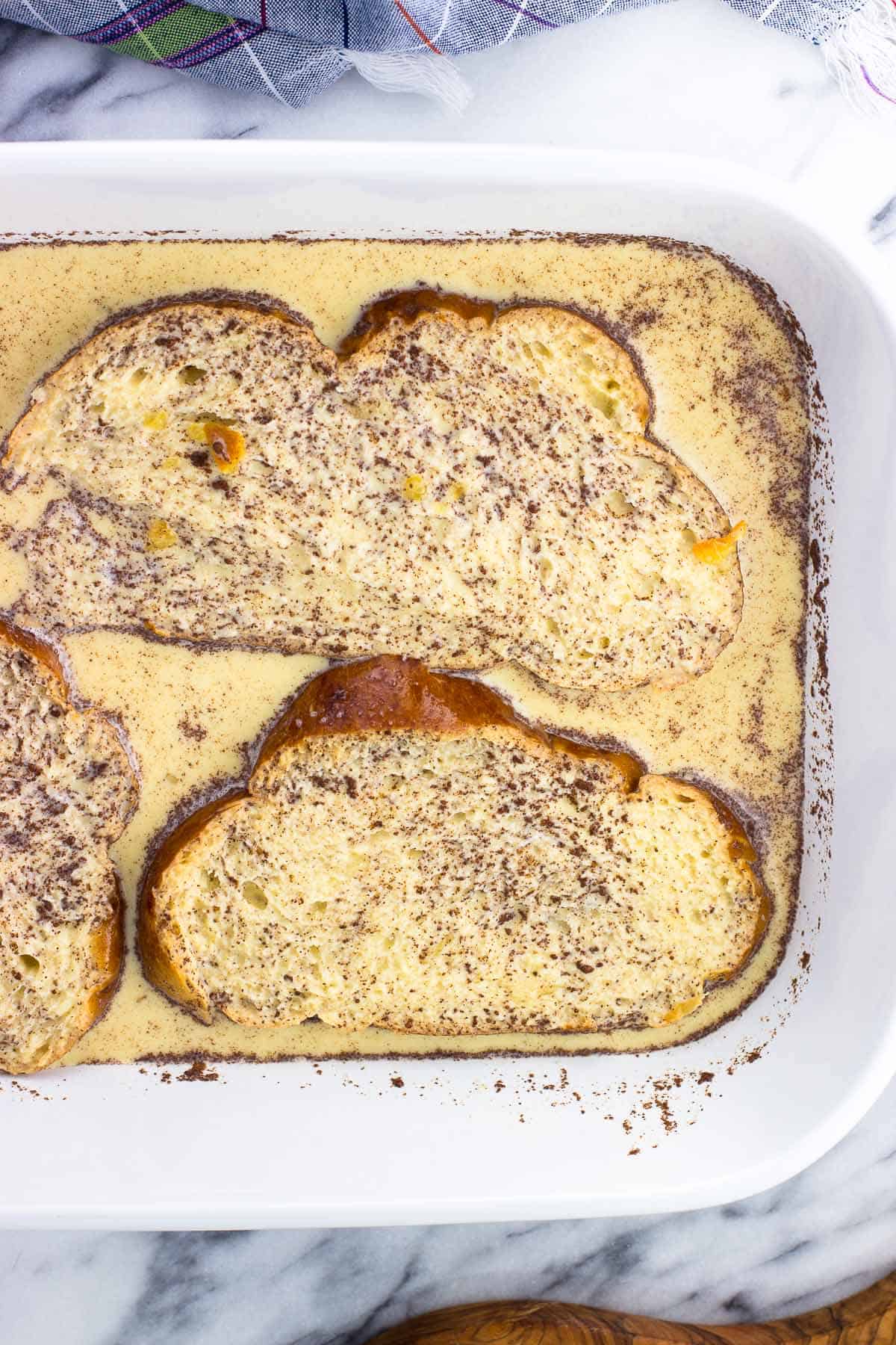 Challah slices soaking in egg mixture in a large rectangular dish.