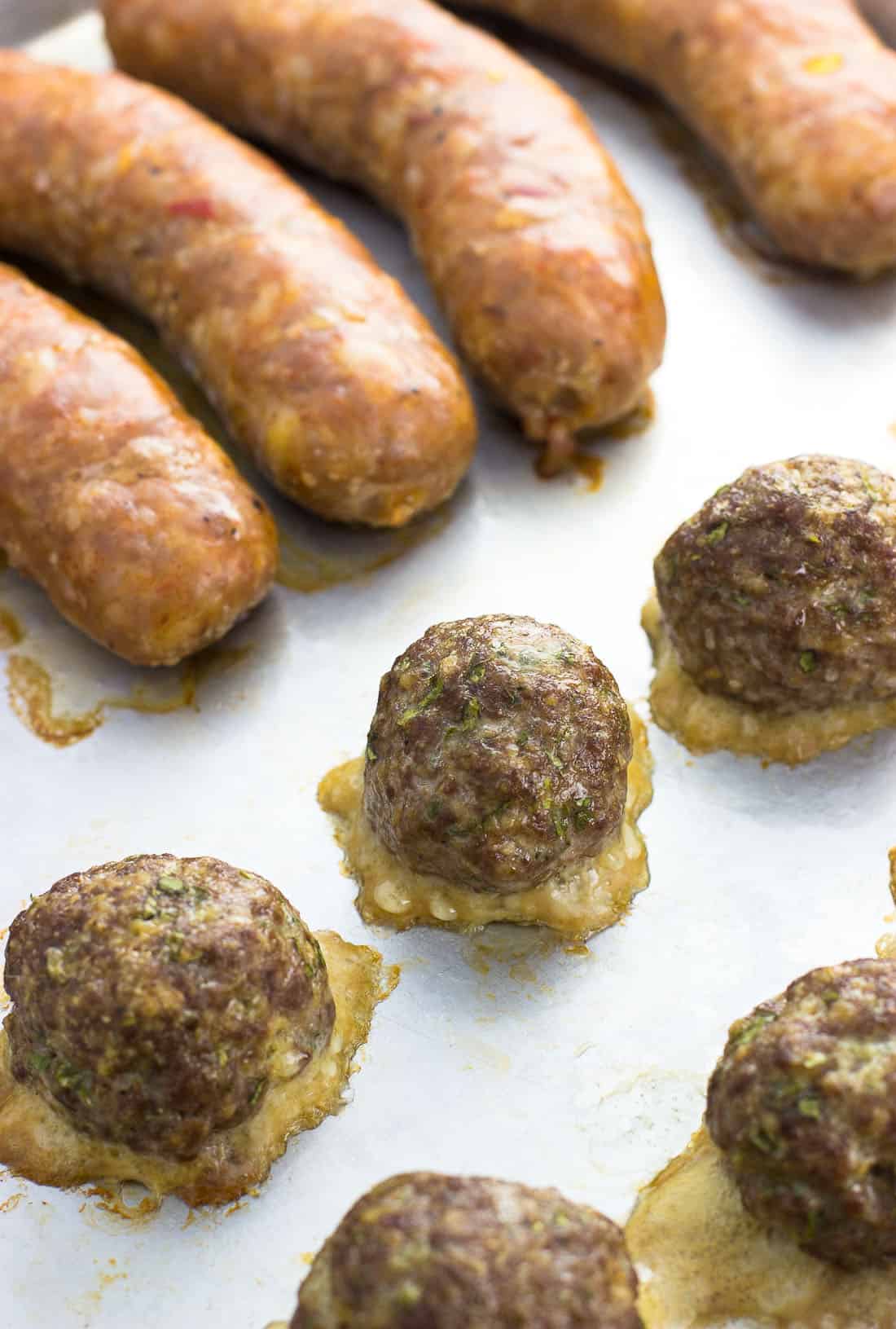 Cooked meatballs and sausages on a baking sheet before being added to the pot of sauce