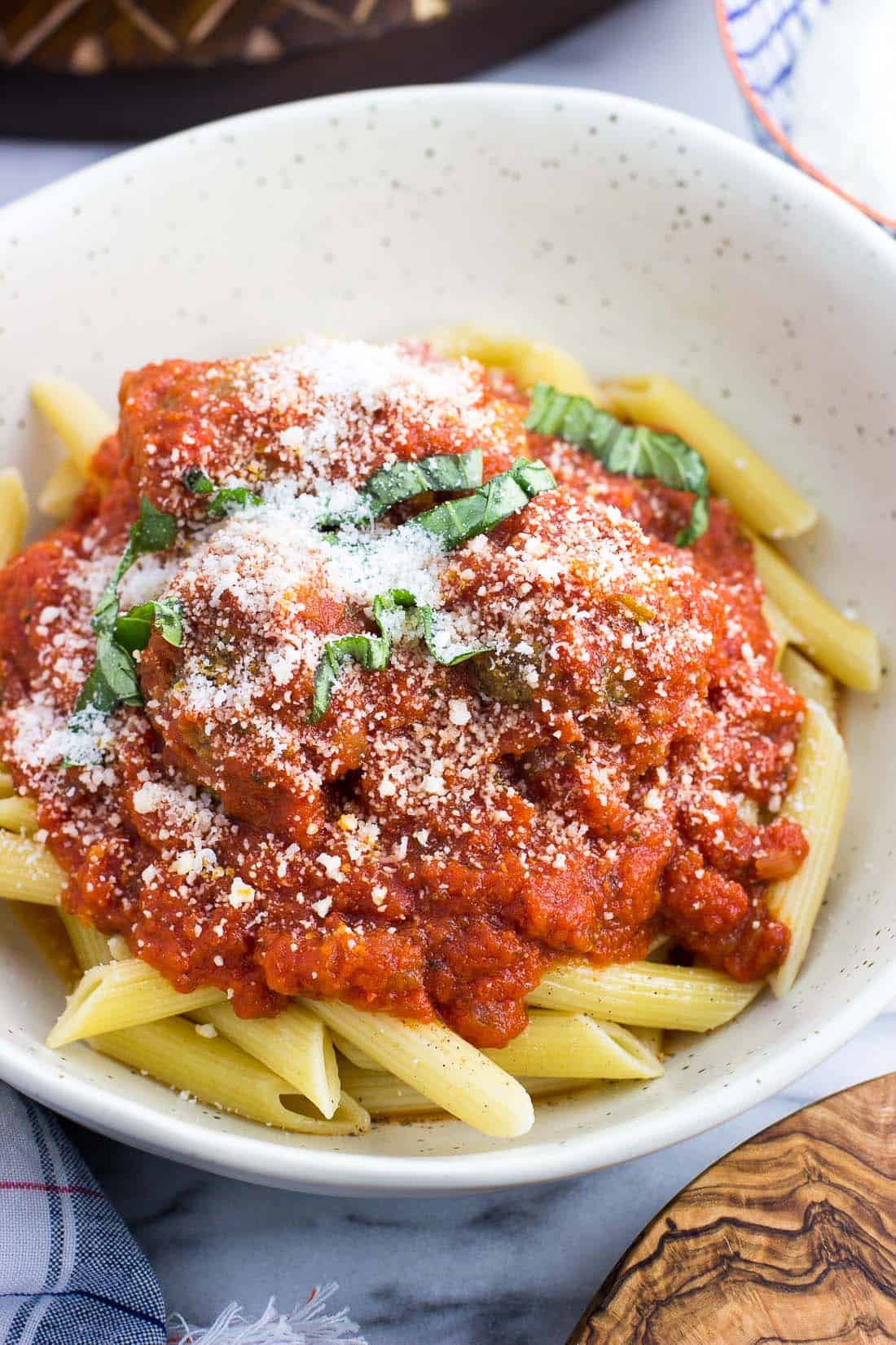 A bowl of pasta and hearty marinara sauce garnished with Parmesan and fresh basil