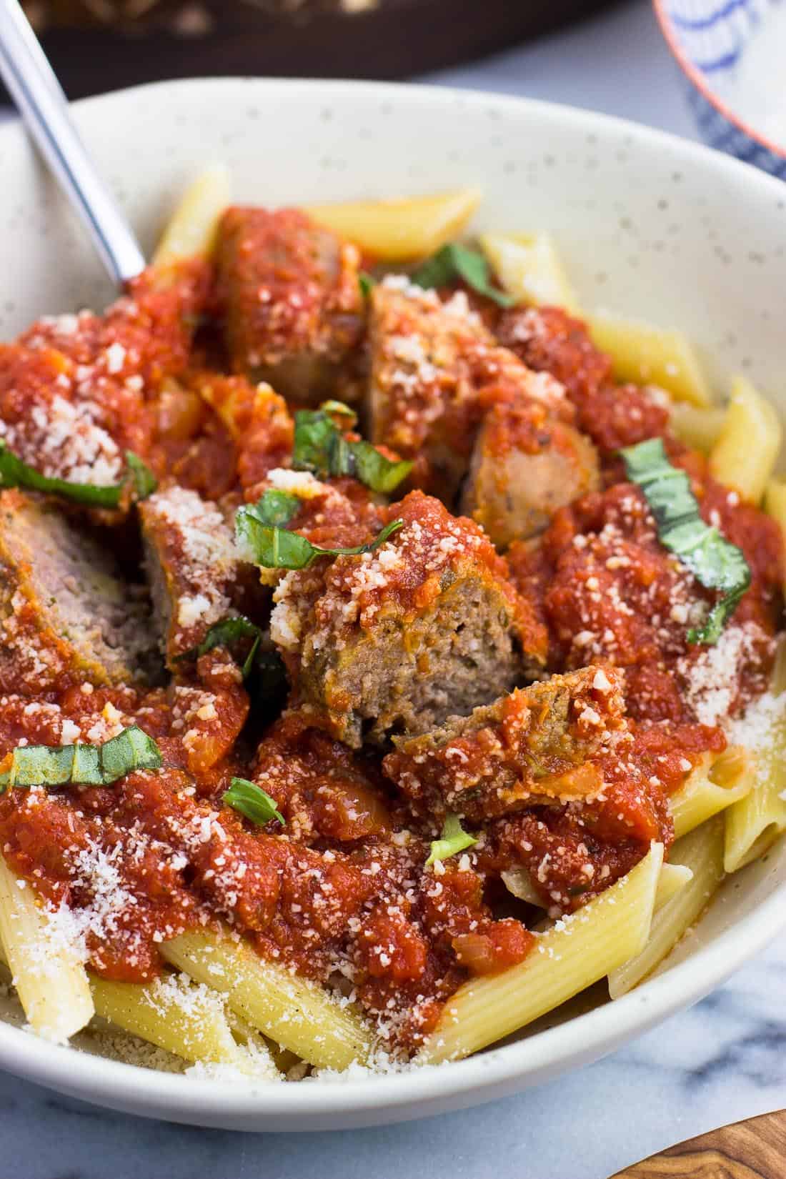 A bowl of Sunday sauce with meatballs and sausage served over penne pasta and garnished with Parmesan