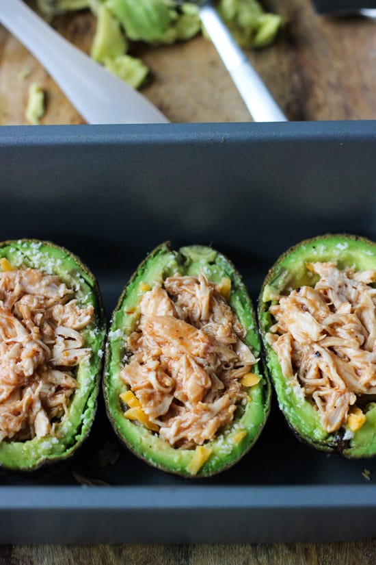 Avocado halves stuffed with cooked pulled chicken in a loaf pan.