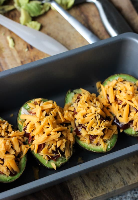 Shredded cheese sprinkled on top of the assembled avocado boats before baking.