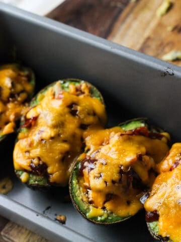 Baked and stuffed avocado boats lined up in a metal loaf pan.